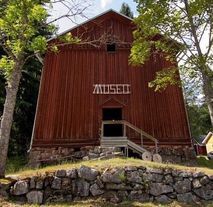 Punainen puurakennus, edessä kivimuuri, rakennuksen edessä ovi, jonka päällä lukee museo