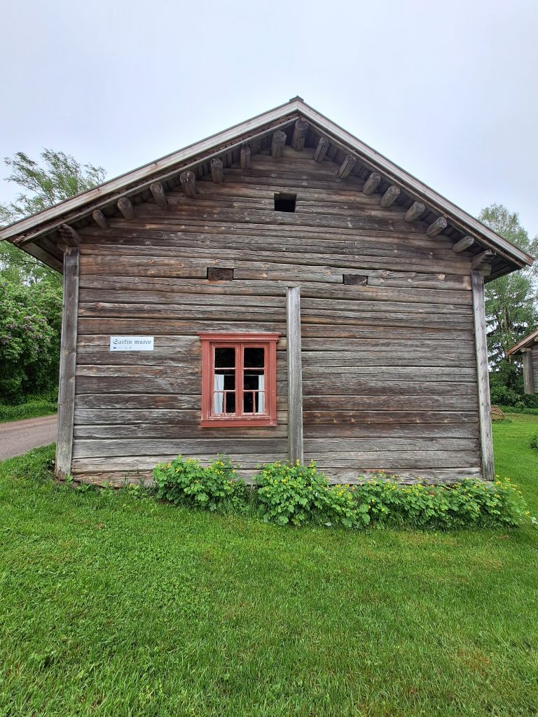 Maalaamaton puinen rakennuksen pääty, jossa punainen ikkuna.