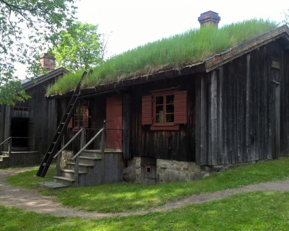 Luostarinmäki Ruohokattoinen maalaamaton puurakennus, jossa puneiset ikkunapuut ja ovi. Edessä portaat ovelle.
