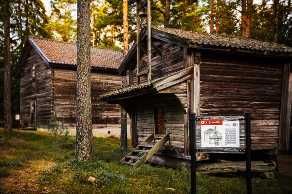 MUSEONMÄKI_0059_1200PX Kaksi museorakennusta metsässä. Edessä opastustaulu, jonka otsikkona vilja-aitta.