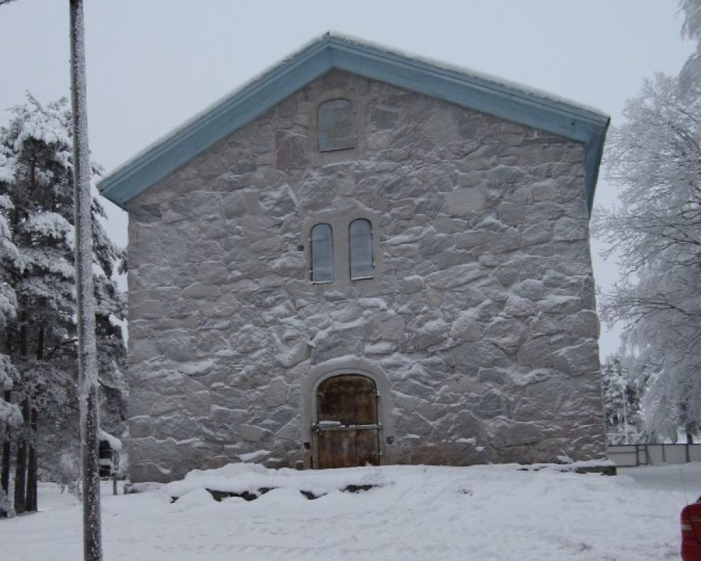 Perttelin kotiseutumuseo on kivisessä sainamakasiinissa. Kuva on otettu talvella, maassa ja rakennuksen seinällä on lunta.