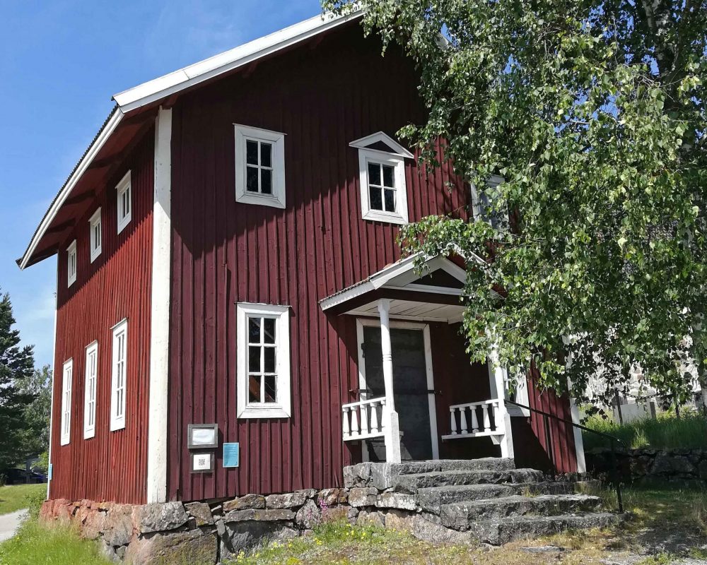 dav Punainen puinen lainamakasiini, jossa on puiset portaat ja katettu kuisti.