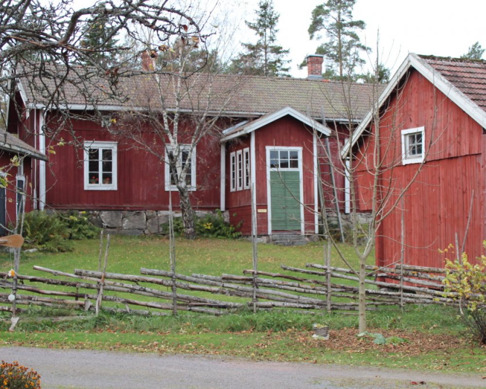 Rymättylän kotiseutumuseo Punainen puutalo sekä punaisia ulkorakennuksia riukuaidan takana.