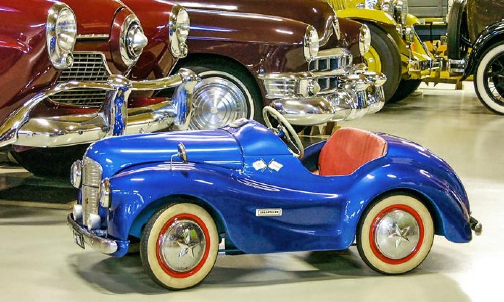 Uudenkaupungin automuseo Taustalla vanhoja autoja, punainen, ruskea ja keltainen. Edessä lapsille tarkoitettu kirkkaan sininen leluauto.