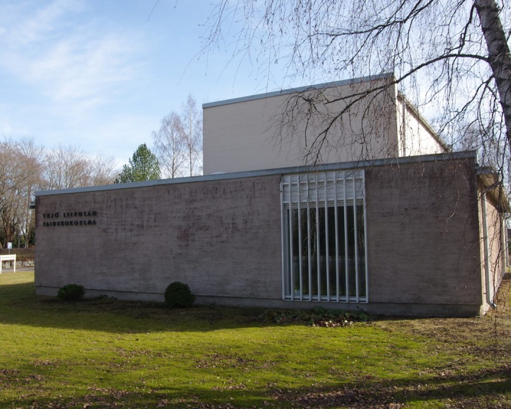 Betoninen harmaa rakennus, jonka oikeassa reunassa on pystyrimainen ikkuna ja vasemmassa reunassa teksti Yrjö Liipolan taidemuseo. Museon edessä on nurmikenttä.